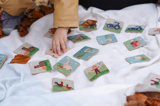 Kind hält Memorykarten aus Holz mit Bauernhof Motiven
